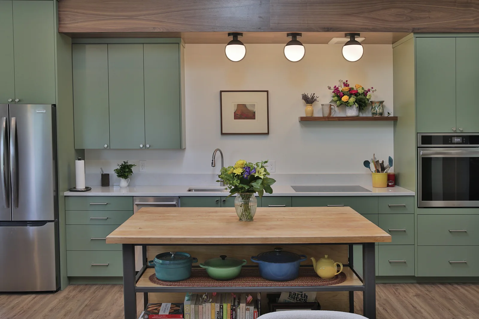 Custom sage green kitchen cabinetry under a walnut ceiling beam with quartz counters