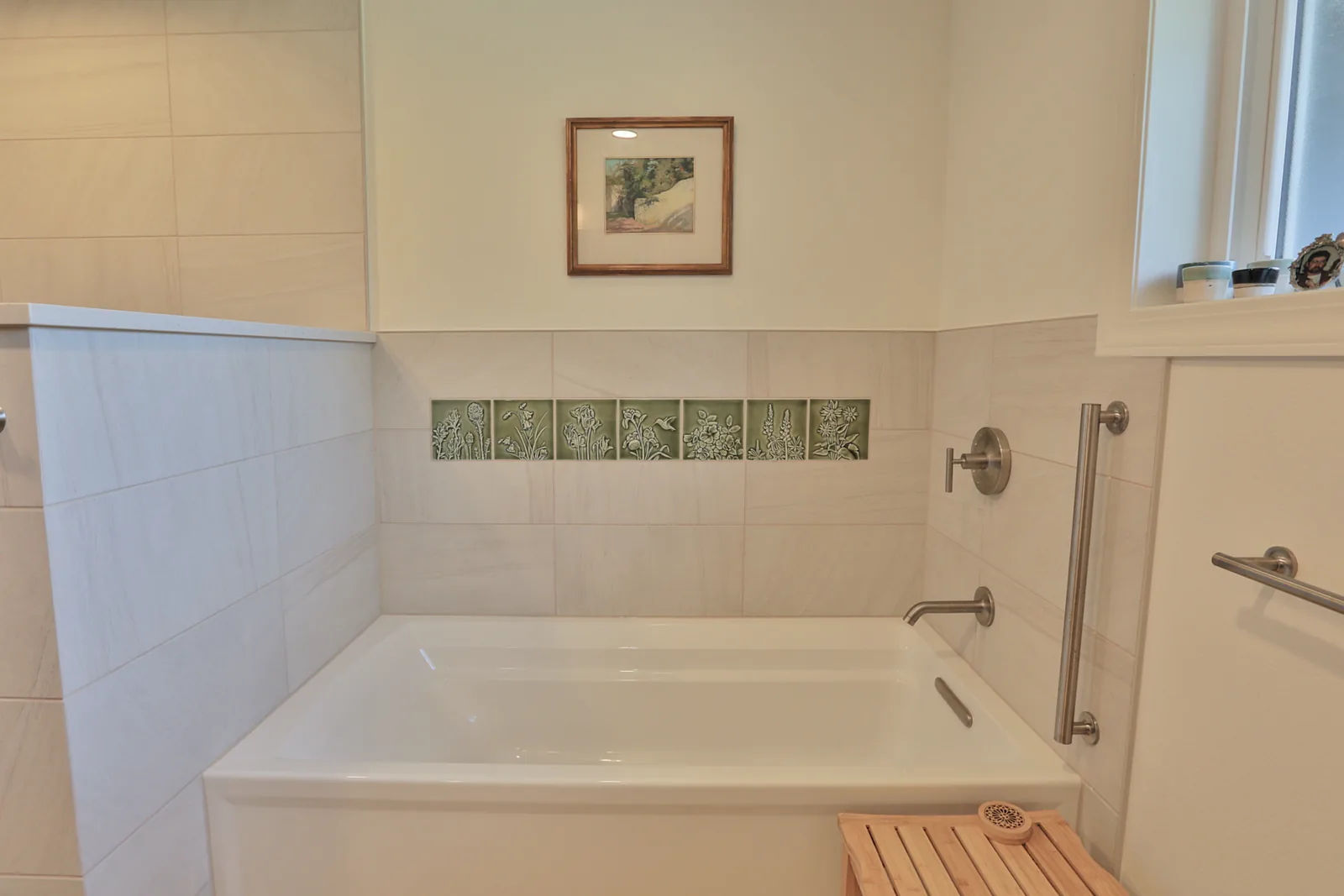 Separate soaking tub with grab bars and a handmade botanical relief tile band
