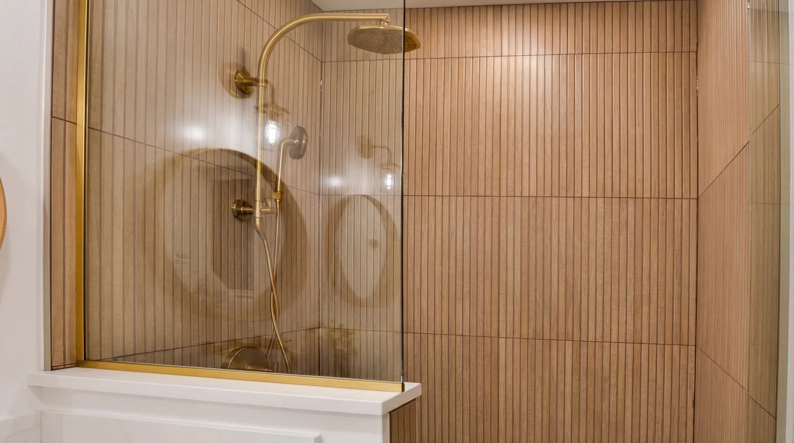 Shower in fluted tile with unlacquered brass fittings and a frameless glass panel