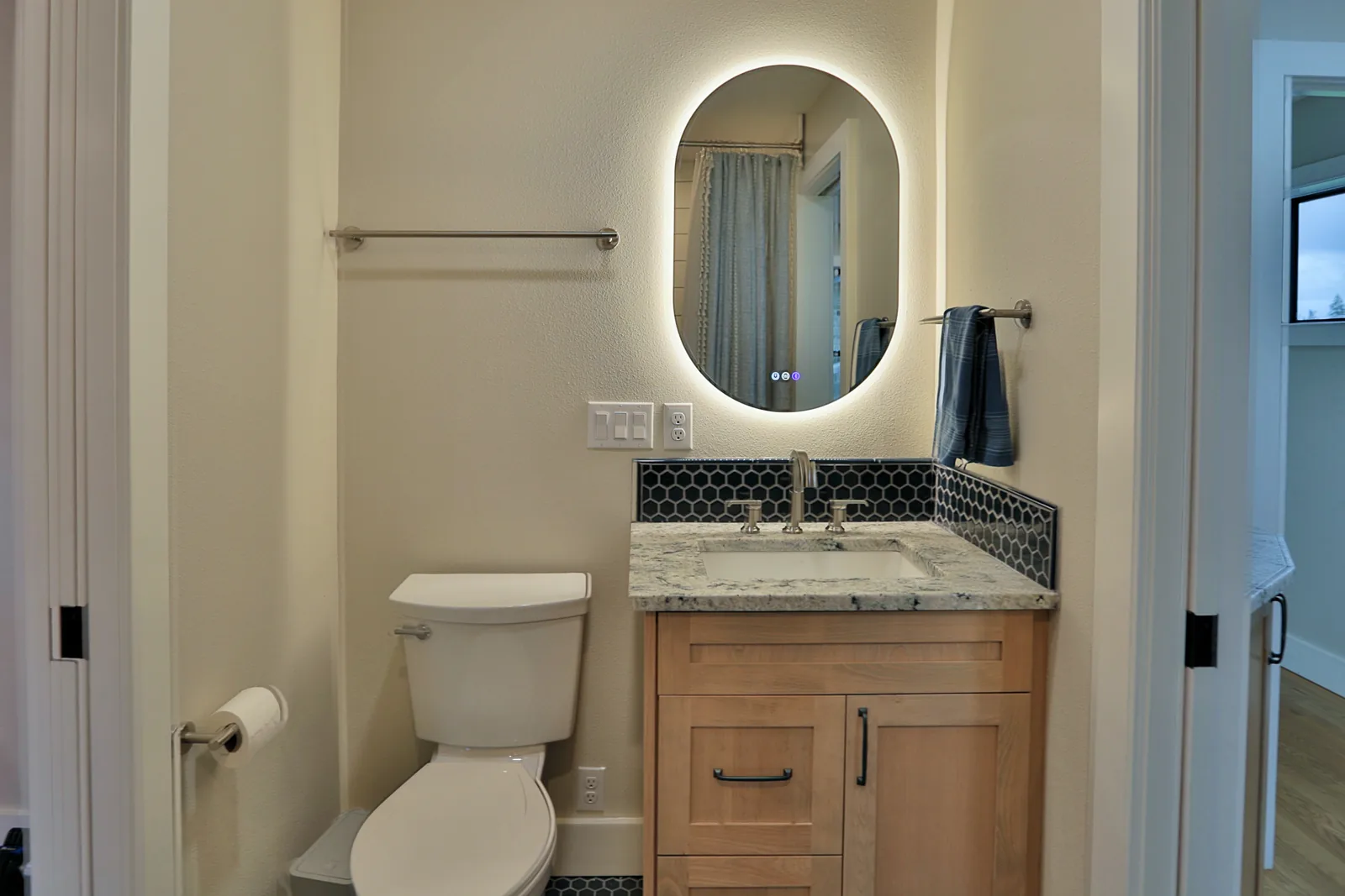 Bathroom with granite counter, navy hex tile backsplash and a backlit mirror