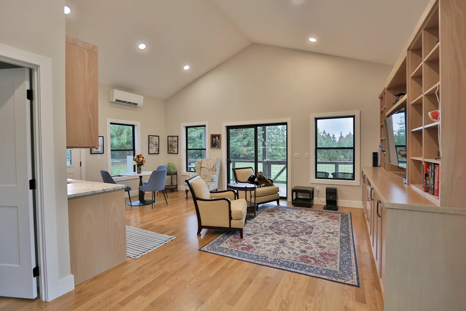 Vaulted great room with built-in white oak shelving and windows onto the pasture