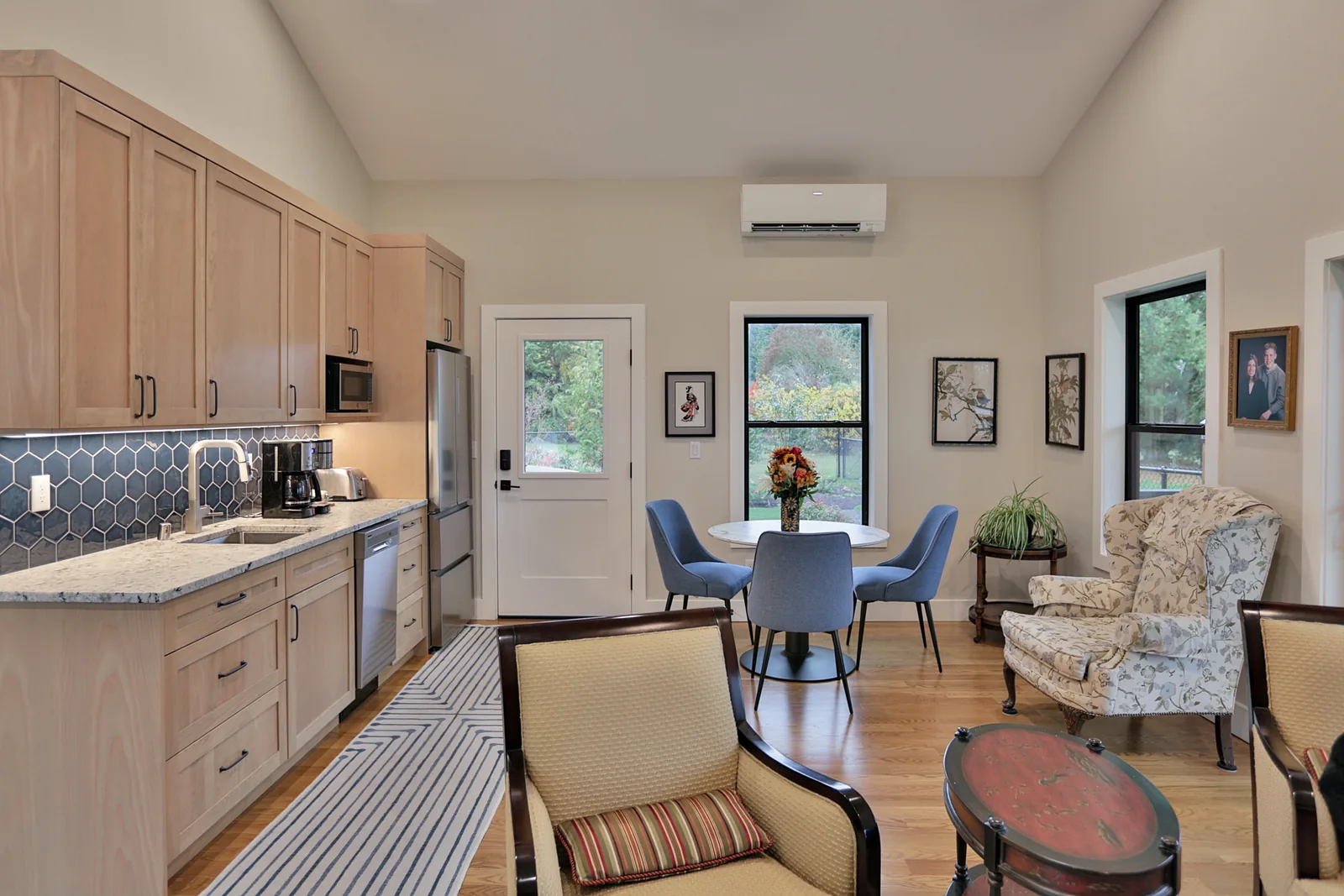 ADU kitchen and living area under a vaulted ceiling with white oak cabinetry and granite counters